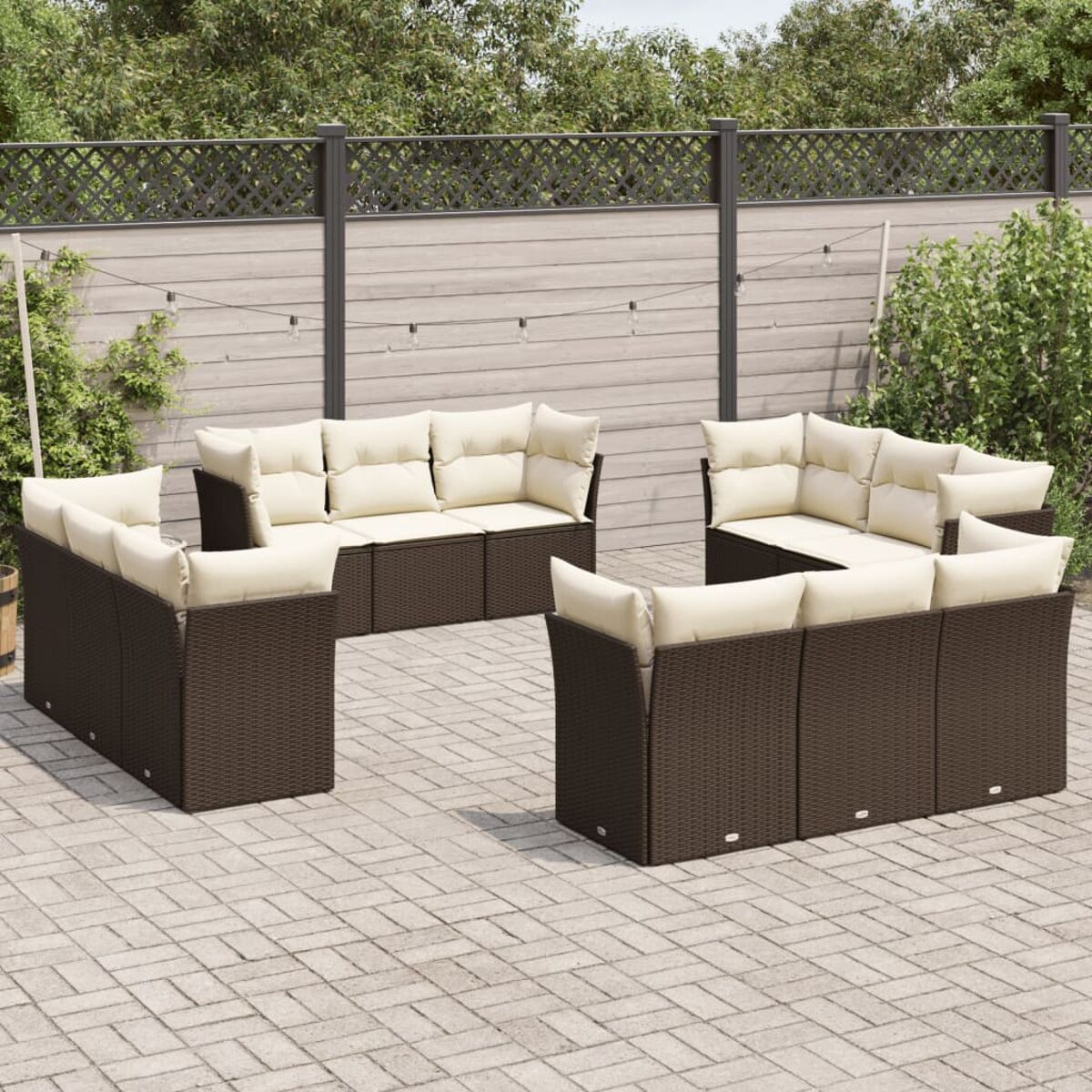 Braunes Outdoor-Sofa-Set aus Korbgeflecht mit beigen Kissen auf einer Backstein-Terrasse. Zaun und Pflanzen im Hintergrund.
