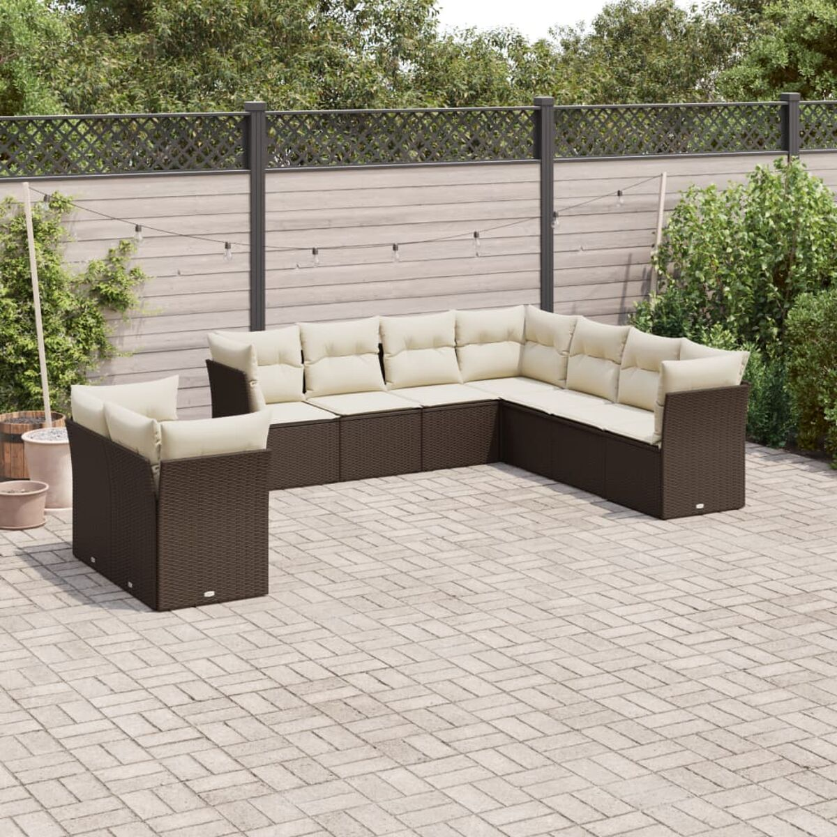Braunes L-förmiges Sofa aus Korbgeflecht mit cremefarbenen Kissen, auf Ziegel-Patio, Holzzaun im Hintergrund.