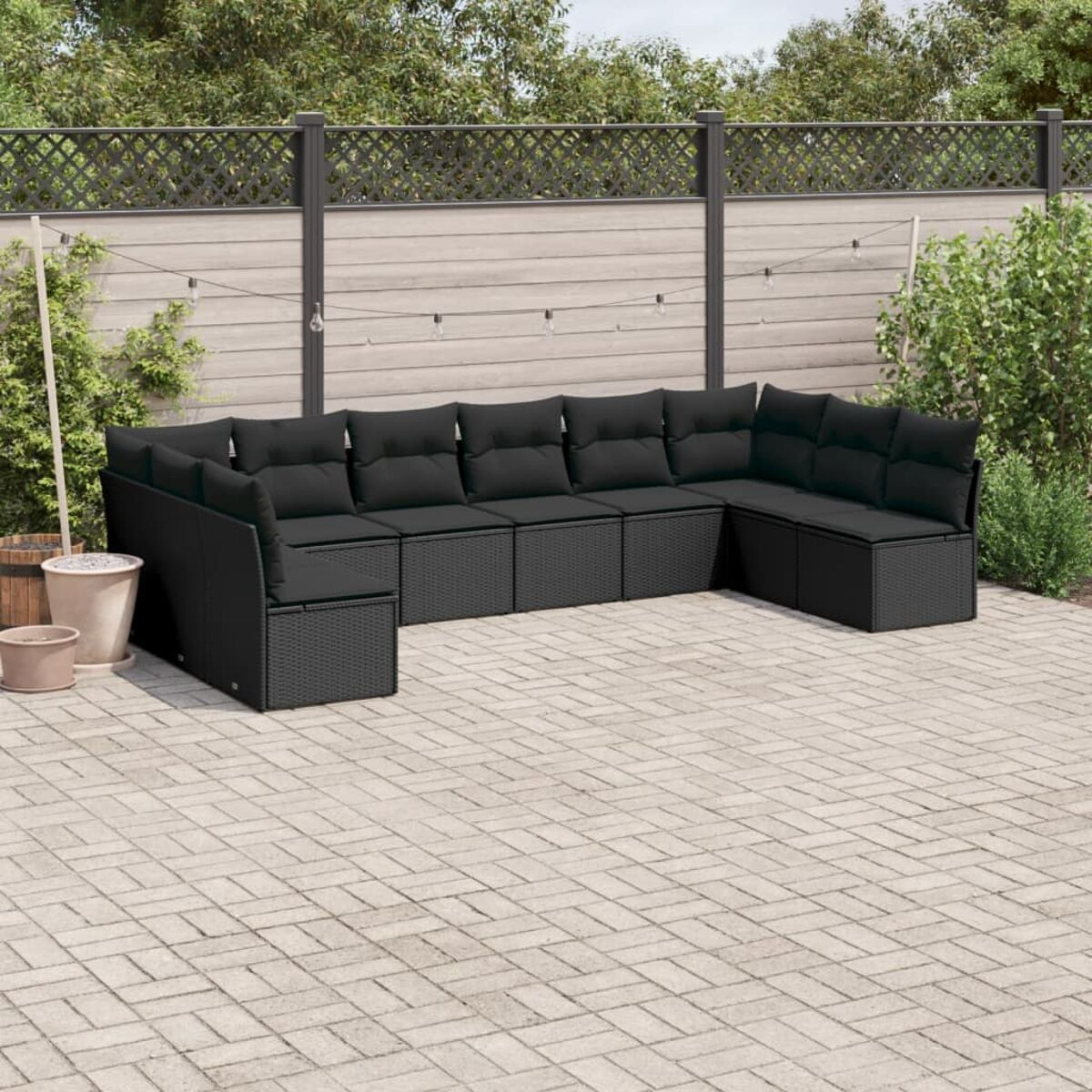 Schwarze Gartenmöbel auf einer Terrasse. Ein großes Ecksofa mit Ziegelmusterboden und grünem Hintergrund.