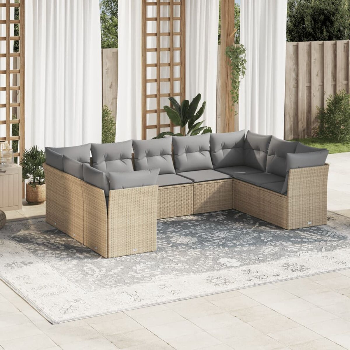Outdoor-Ecksofa aus Korbgeflecht mit grauen Kissen auf einem gemusterten Teppich, mit Vorhängen und Pflanzen im Hintergrund.