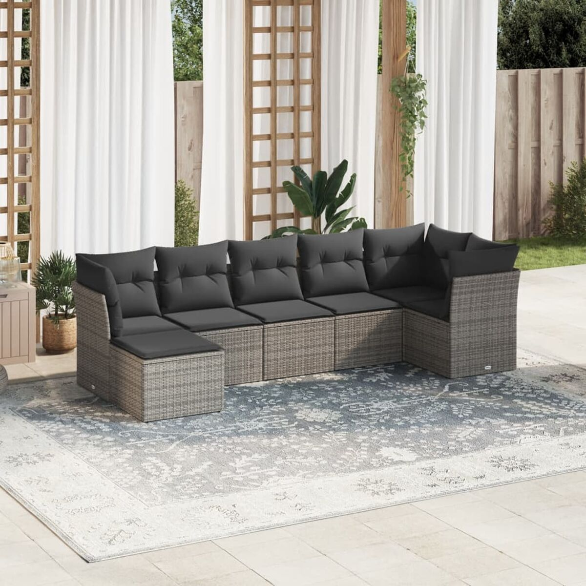 Terrasse mit Rattan-Ecksofa. Graue Kissen auf dem Sofa. Weiße Vorhänge und ein Teppich im Hintergrund.