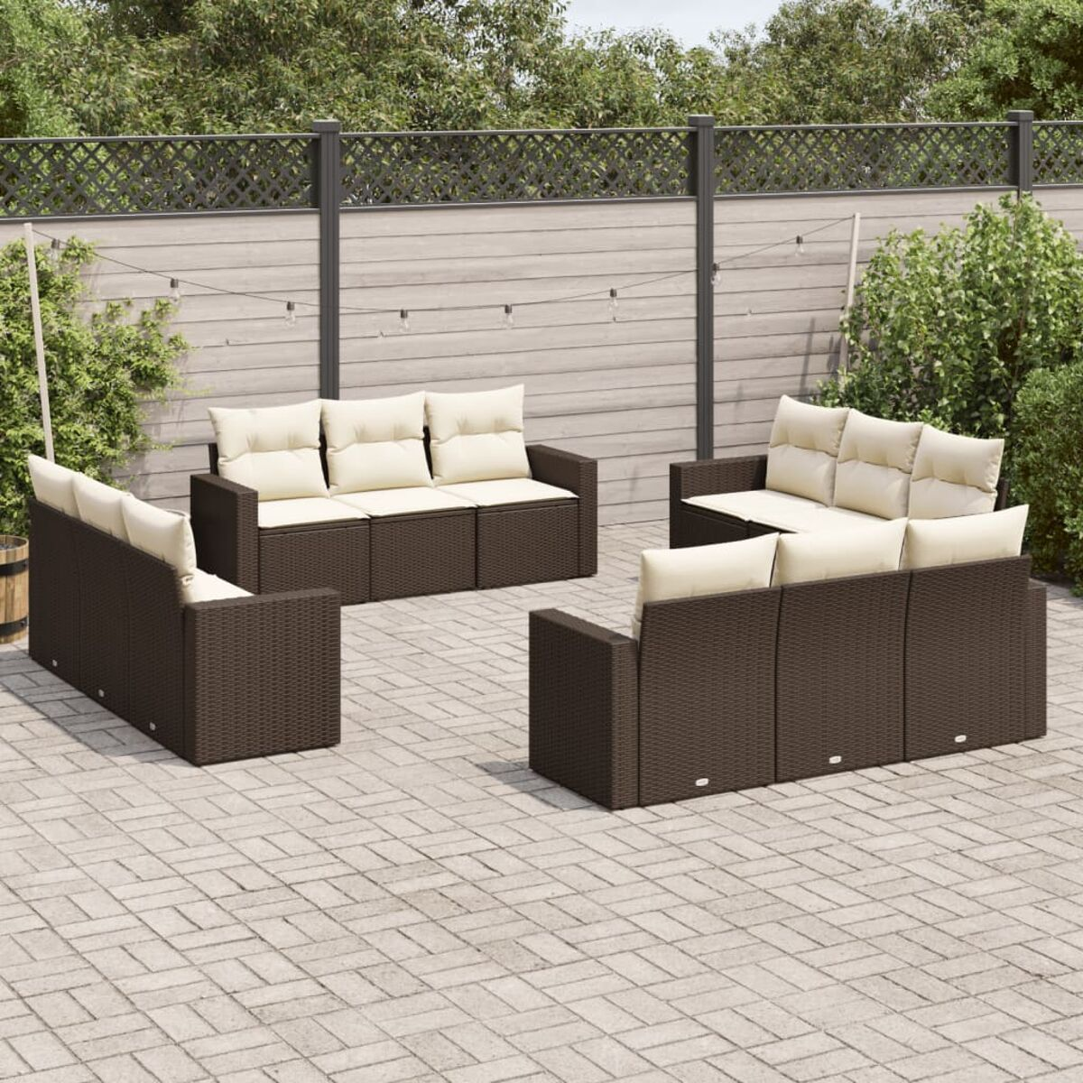 Outdoor-Sitzgruppe. Braune Sofas aus Weide mit cremefarbenen Kissen. Gepflasterte Terrasse mit Holzzaun.