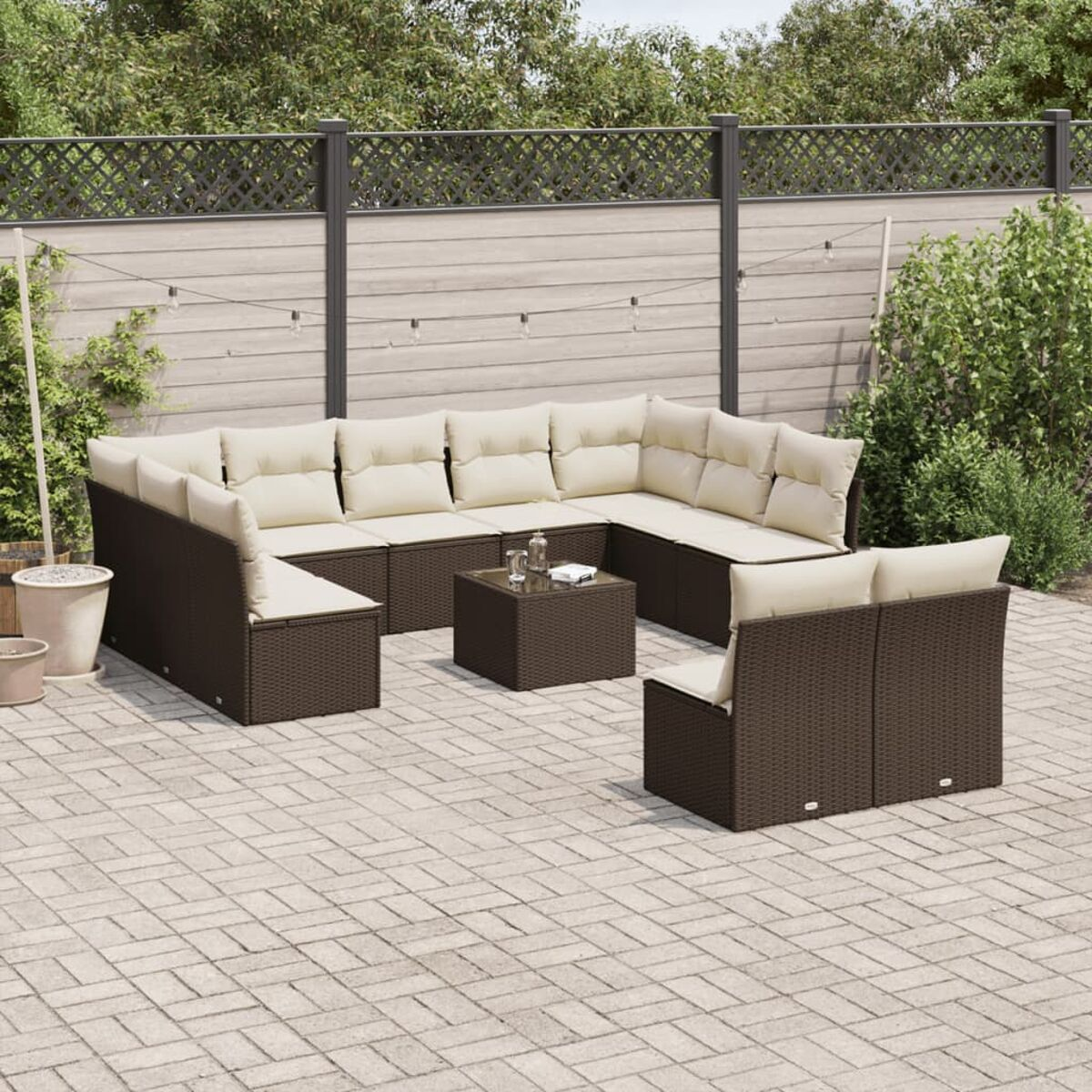Un set di divani angolari in vimini marrone con cuscini color crema, tavolo e piante su un patio.