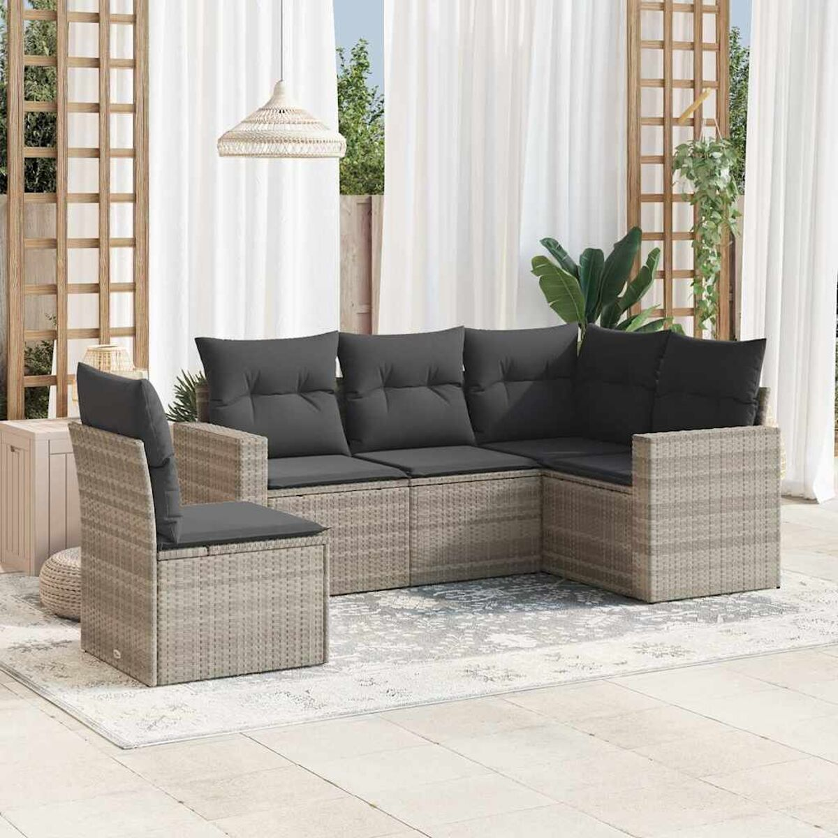 Divano angolare in rattan con cuscini grigi e una sedia. Lo sfondo include tende, tappeto e luce.