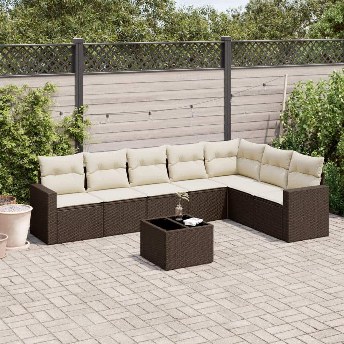 Divano componibile in rattan marrone per esterni con cuscini color crema e tavolino.