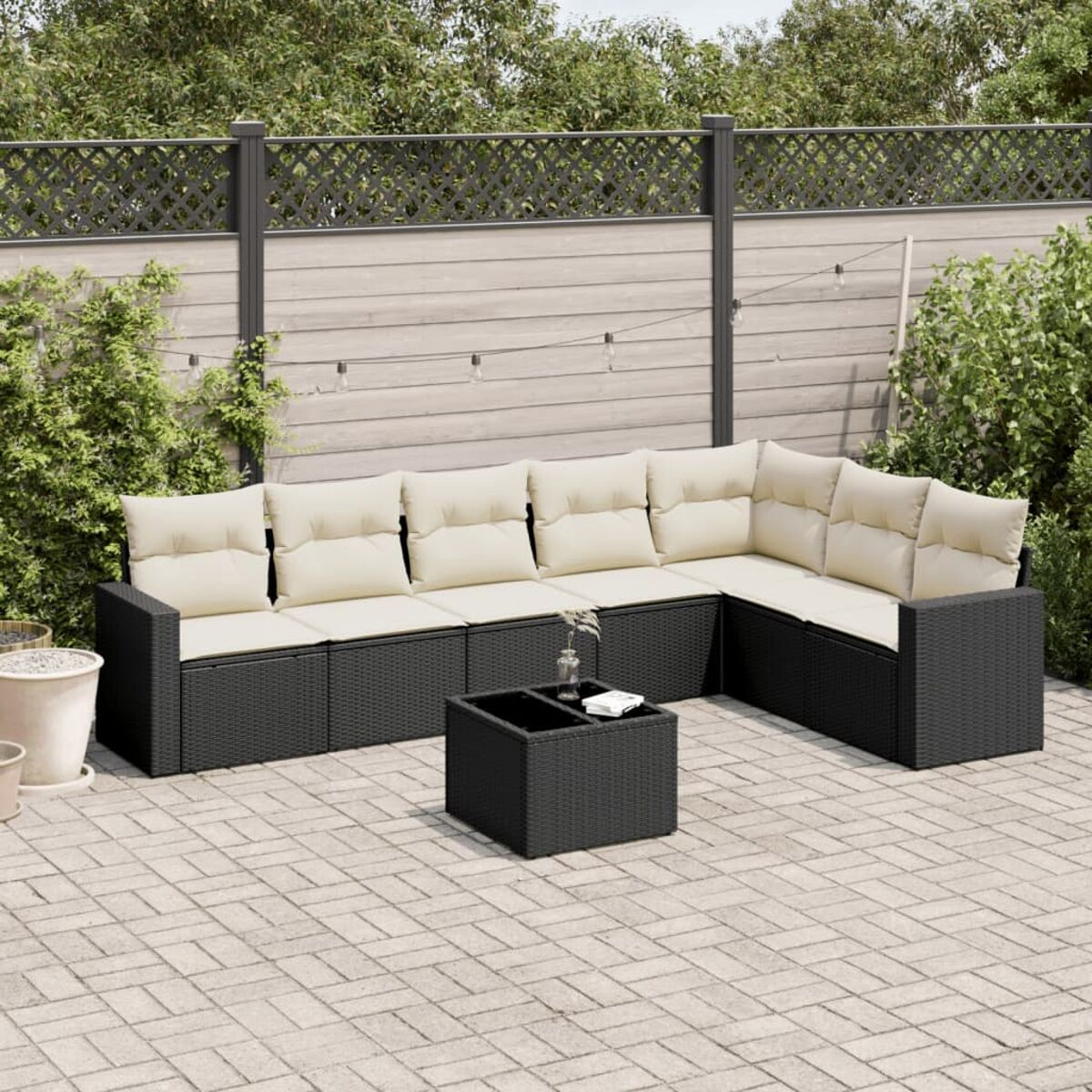 Schwarzes Outdoor-Ecksofa mit cremefarbenen Kissen und einem quadratischen Tisch auf einer Terrasse.