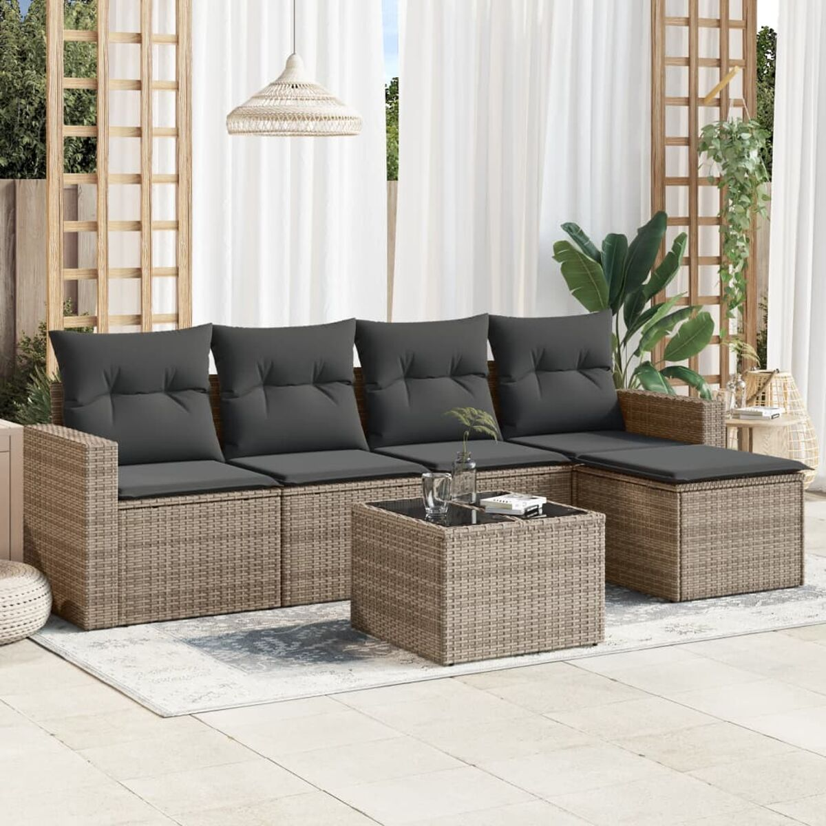 Korbmöbelsofa mit grauen Kissen und einem Tisch auf einem Teppich, weiße Vorhänge dahinter.