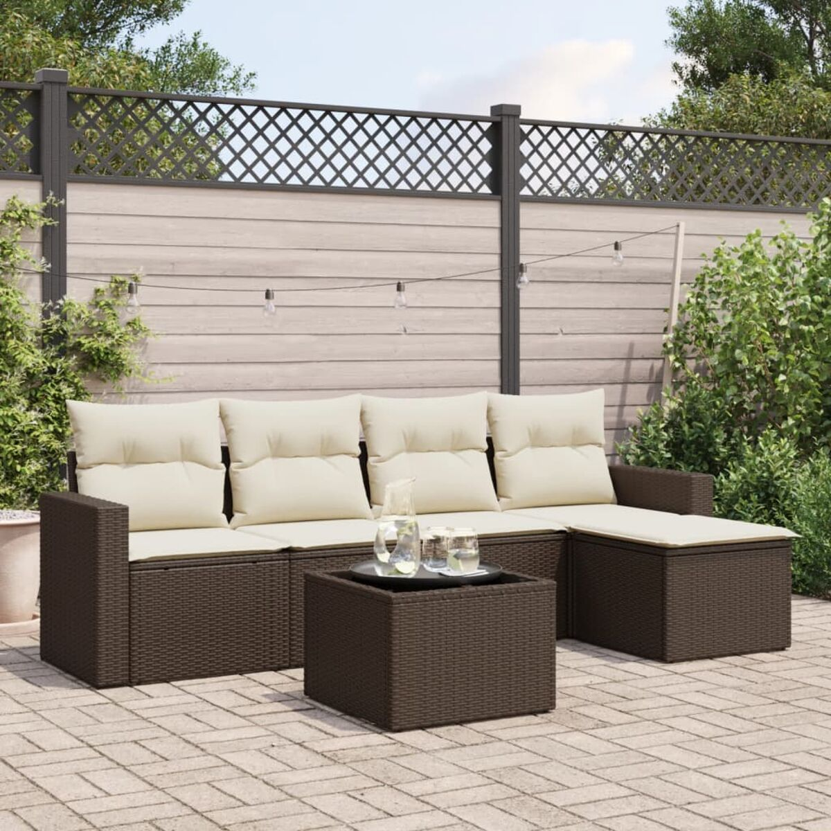 Braunes Sofa-Set aus Korbgeflecht mit cremefarbenen Kissen und Couchtisch. Backstein-Patio, Gartenhintergrund.