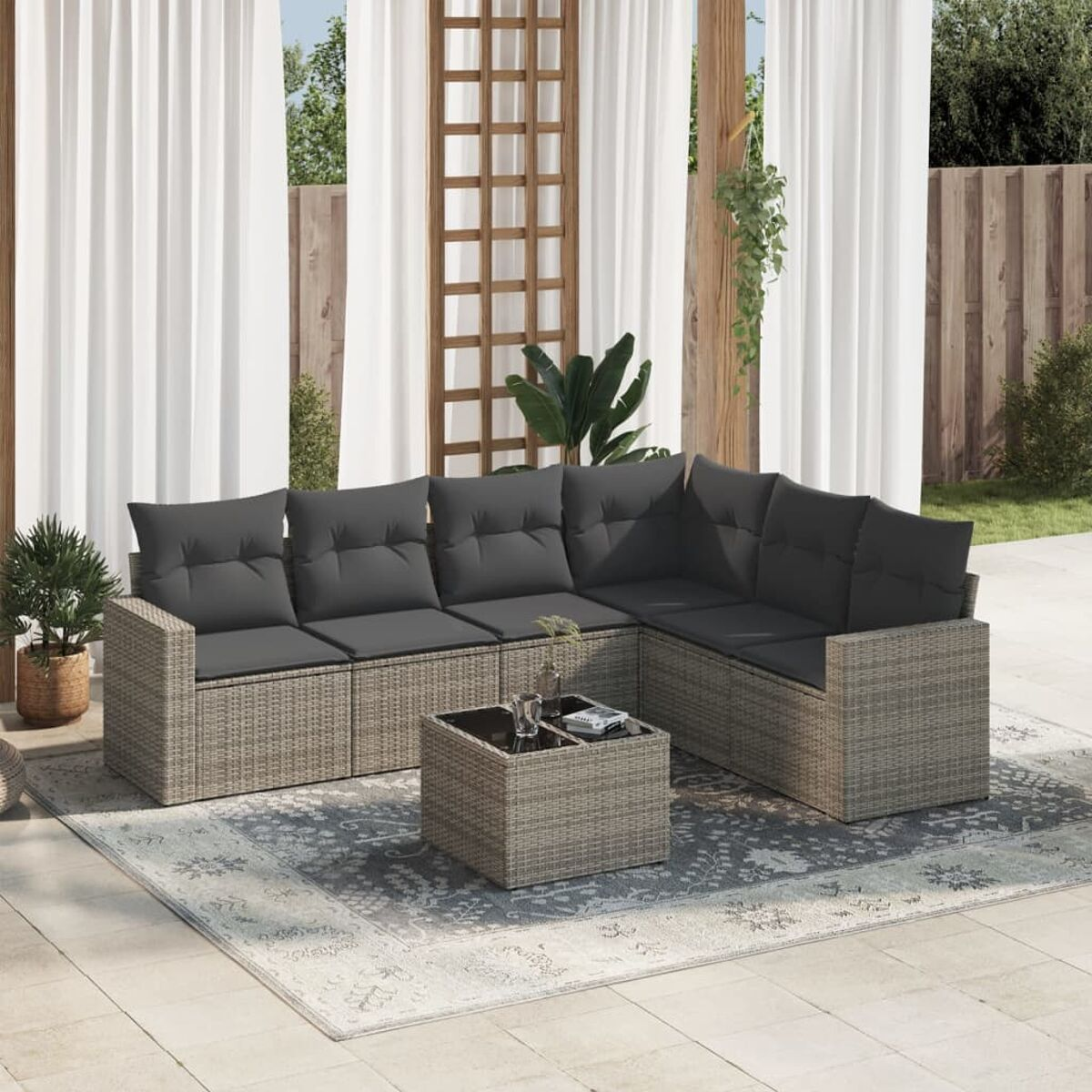 Graues Ecksofa aus Korbgeflecht mit dunkelgrauen Kissen, Couchtisch und Musterteppich.