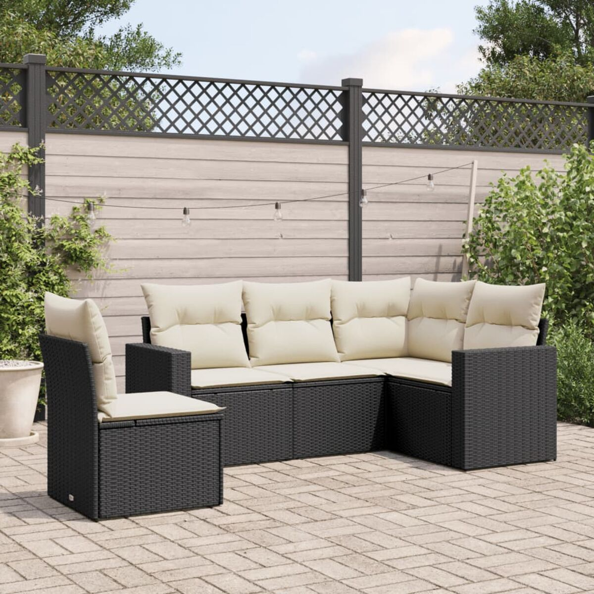 Schwarzes Korbgeflecht-Ecksofa mit cremefarbenen Kissen und passendem Stuhl. Terrasse mit Pflanzen.
