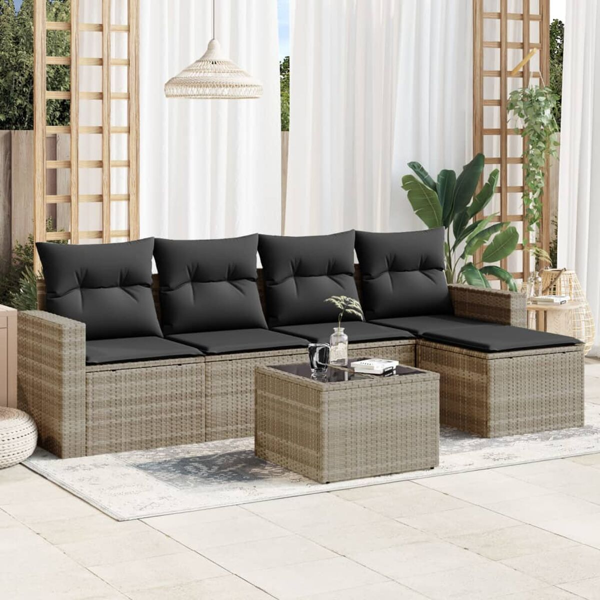 Divano componibile in rattan con cuscini grigi e tavolo. Su tappeto, con tende.