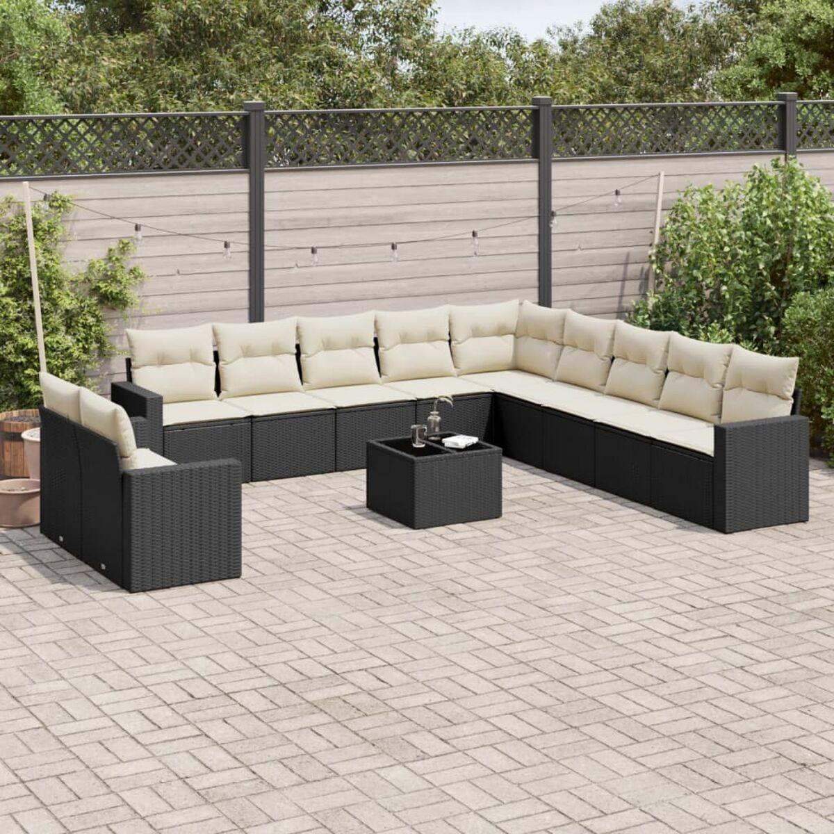 Schwarzes Ecksofa aus Korbgeflecht mit beigen Kissen und einem schwarzen Tisch. Auf einer Ziegelterrasse.