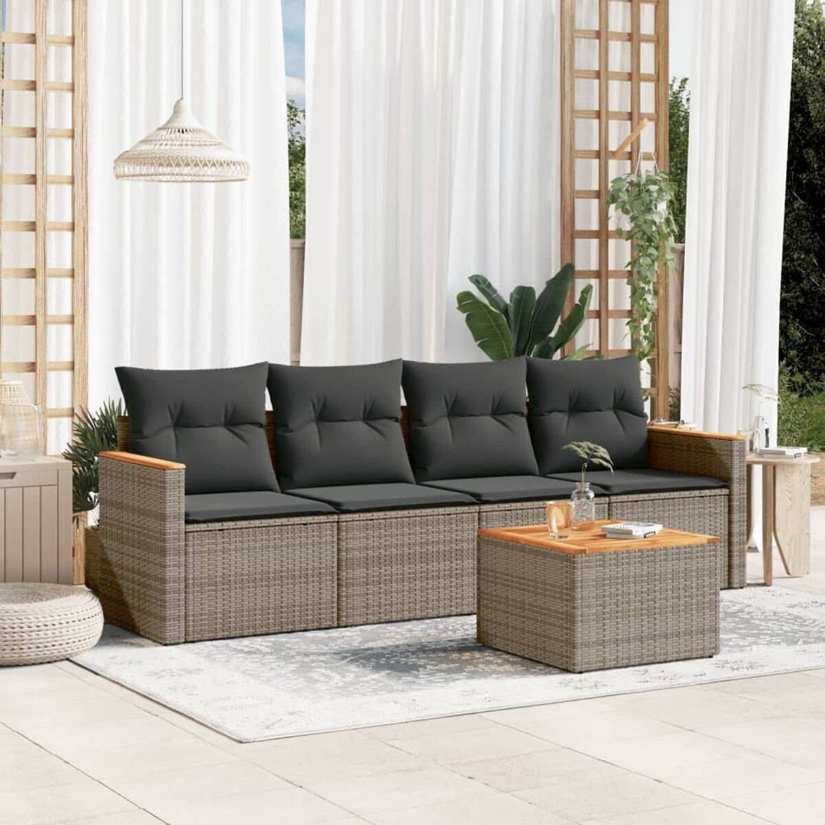 Rattan-Sofa-Set, graue Kissen, Holzarmlehnen, Couchtisch. Auf einer Terrasse mit Vorhängen im Hintergrund.