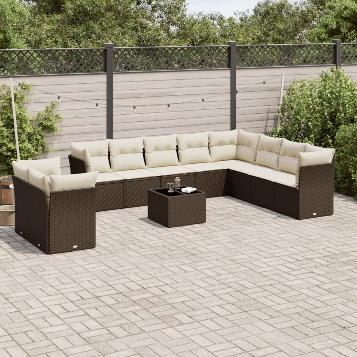 Set patio esterno. Mobili in vimini marrone con cuscini beige. Tavolo al centro. Recinto in legno dietro.