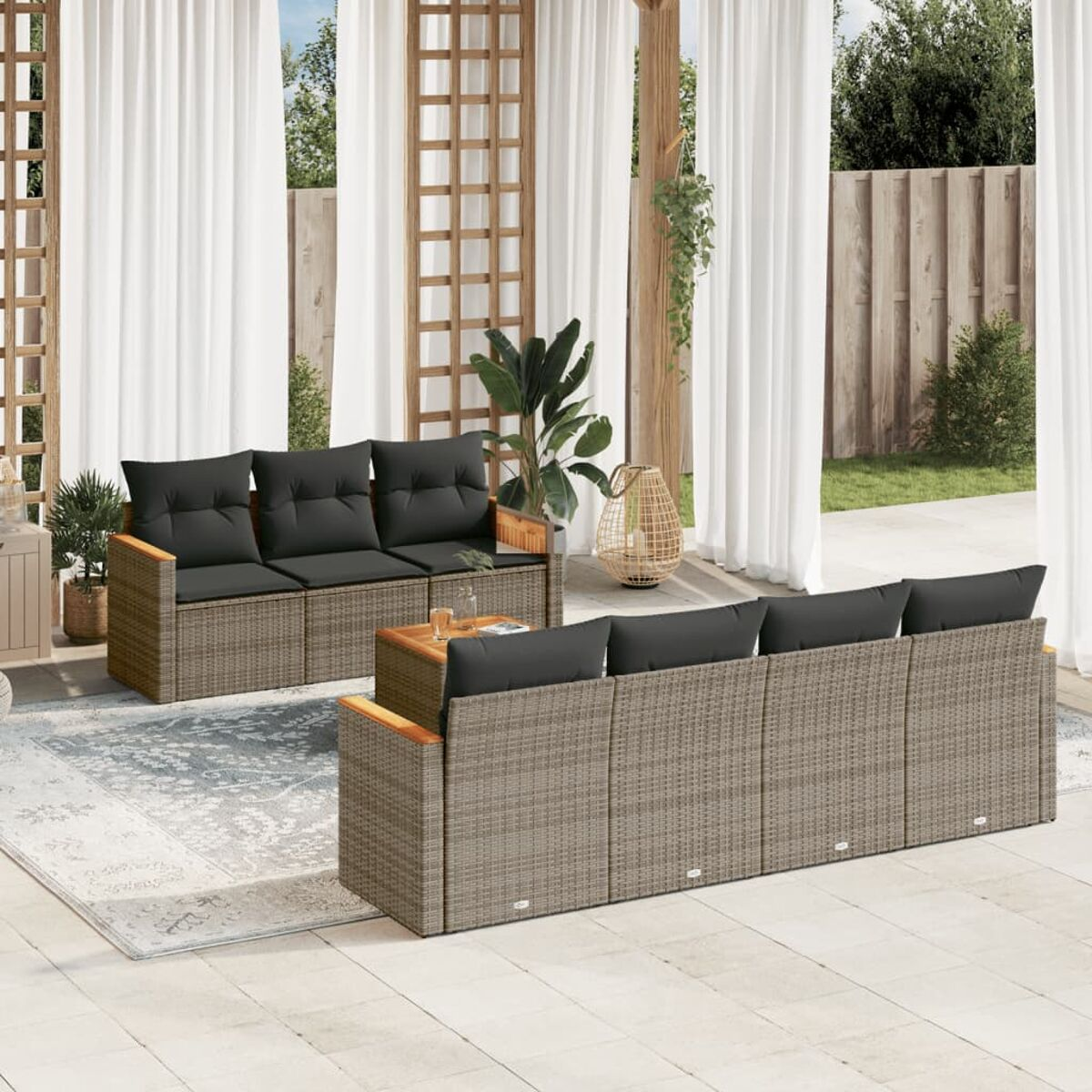 Rattan-Sofaset mit schwarzen Kissen auf einer Terrasse, mit weißen Vorhängen im Hintergrund.