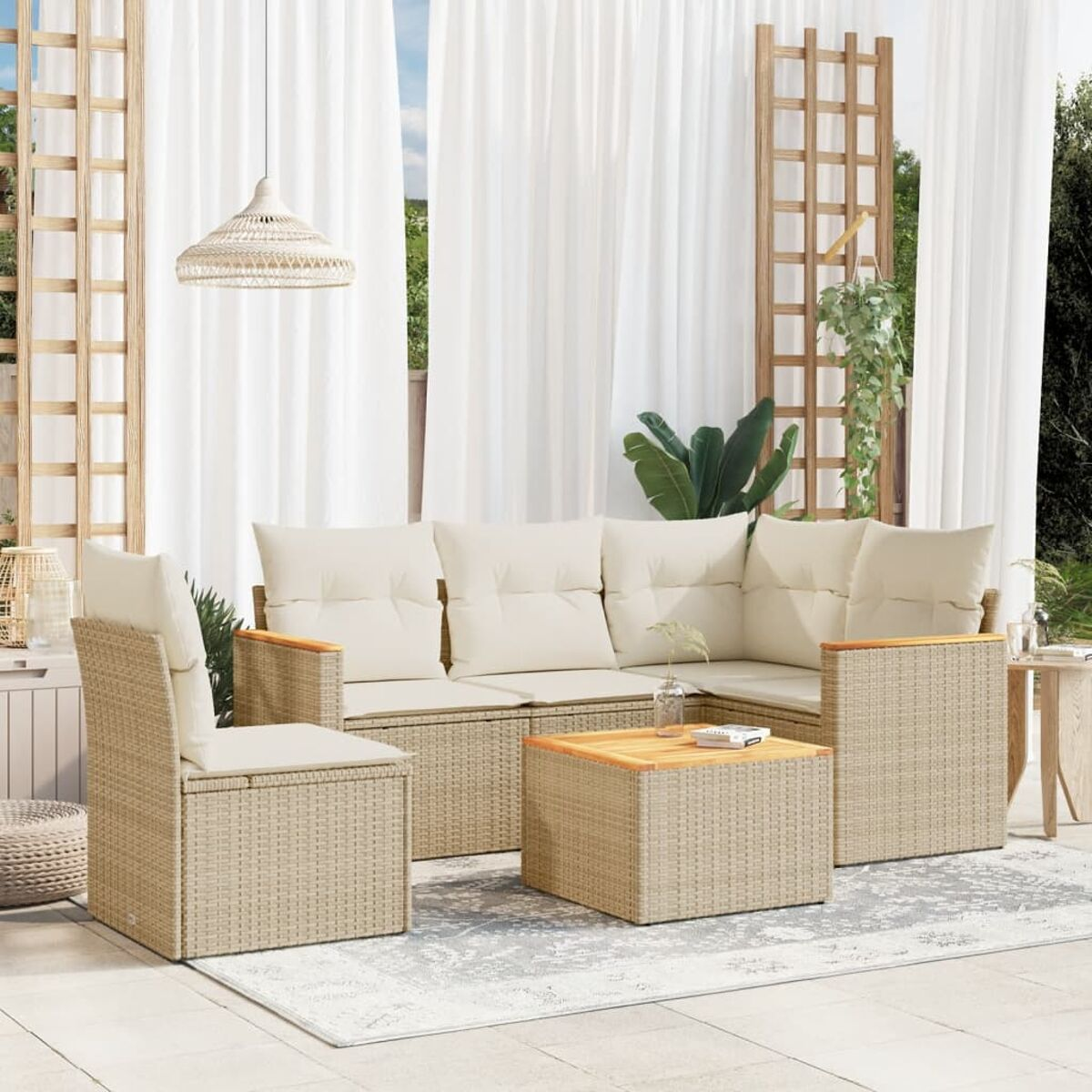 Outdoor-Geflecht-Sofagarnitur mit beigefarbenen Kissen und einem Couchtisch. Weiße Vorhänge, Pflanzen.