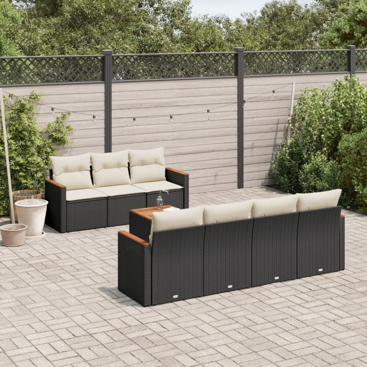 Terrassenset: schwarze Korbsessel, beige Kissen, Holzarmlehnen und Tisch auf Ziegelpflaster.