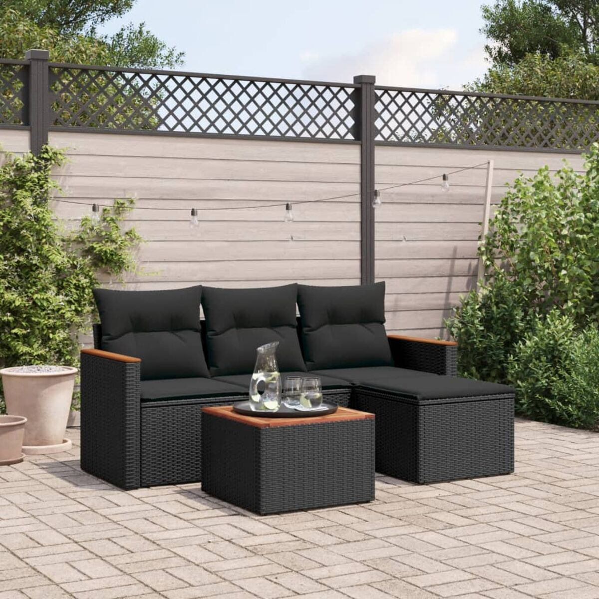 Schwarzes Korbmöbel-Set mit schwarzen Kissen, einem Tisch und Pflanzen. Auf einer Ziegelterrasse.