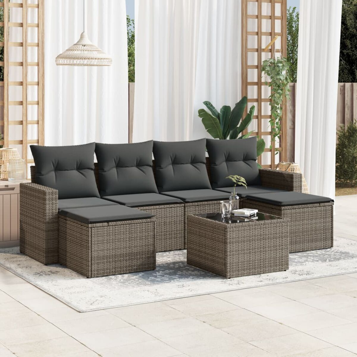Outdoor-Sofa mit grauen Kissen und Couchtisch auf einem Teppich, in der Nähe weißer Vorhänge.