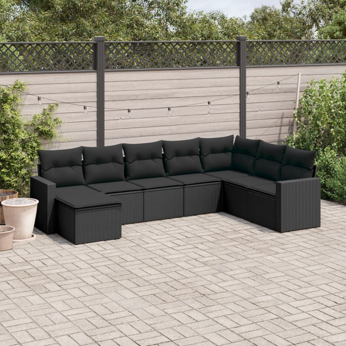 Schwarzes Korbmöbel-Set für die Terrasse mit schwarzen Kissen. Sofa, Ottomane und Beistelltisch. Graue Ziegel und Zaun.
