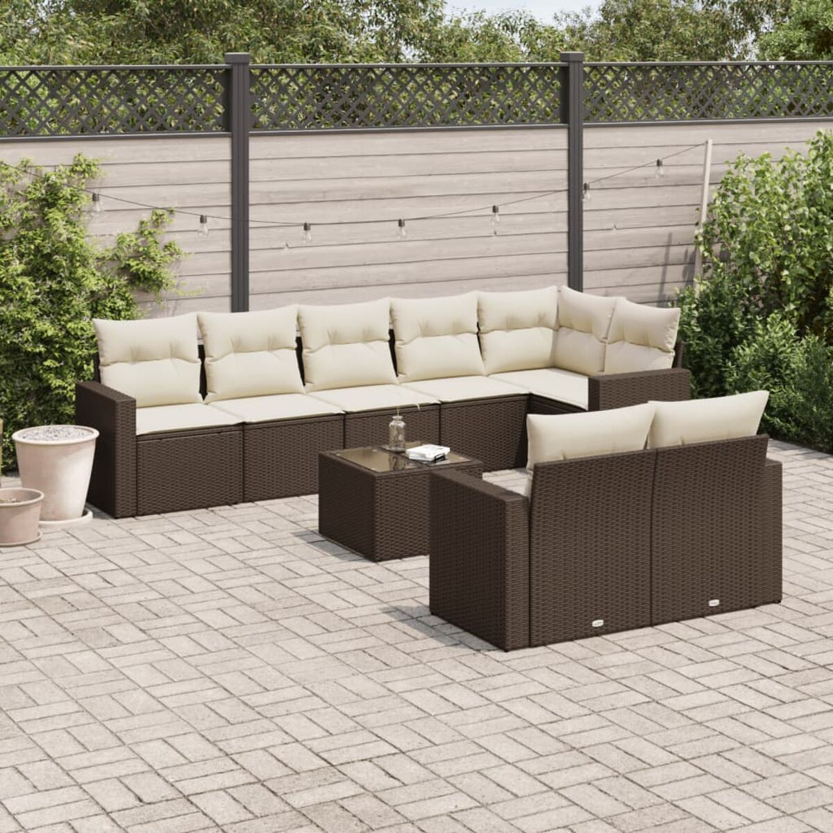 Divano angolare in rattan marrone con cuscini color crema e tavolino su un patio. Piante sullo sfondo.