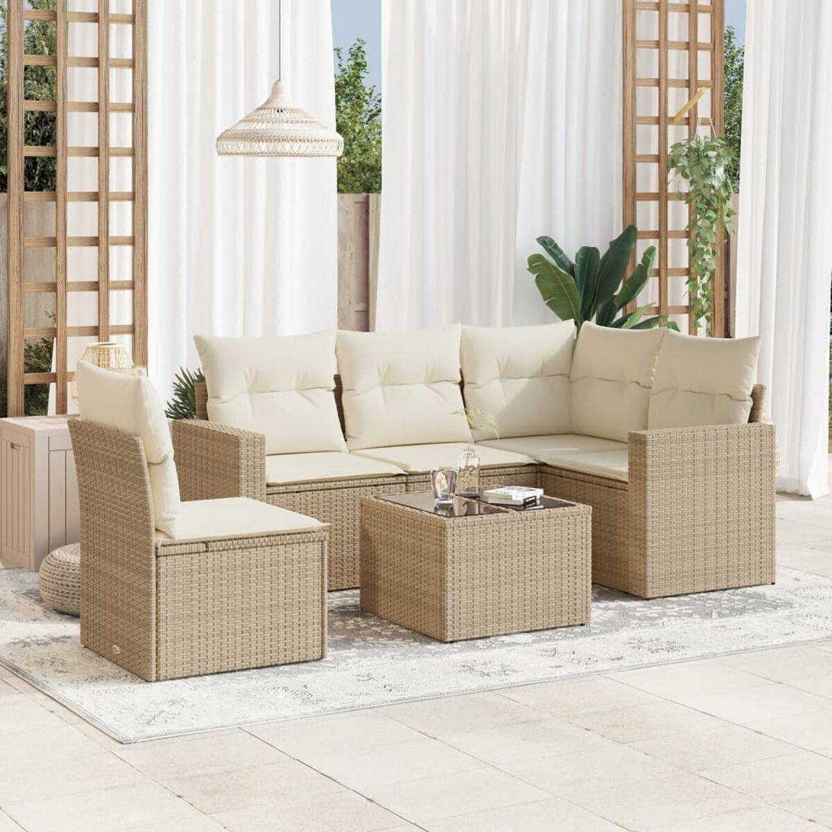 Outdoor-Rattan-Sofagarnitur mit beigen Kissen, Tisch und Stuhl. Weiße Vorhänge im Hintergrund.
