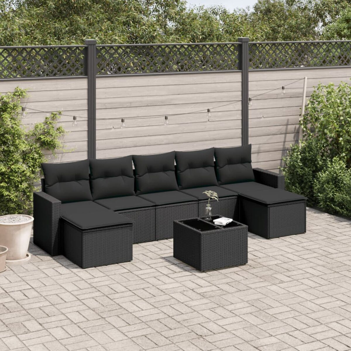 Schwarzes Korbsofa-Set für den Außenbereich mit schwarzen Kissen und einem Couchtisch auf einer Ziegelterrasse.