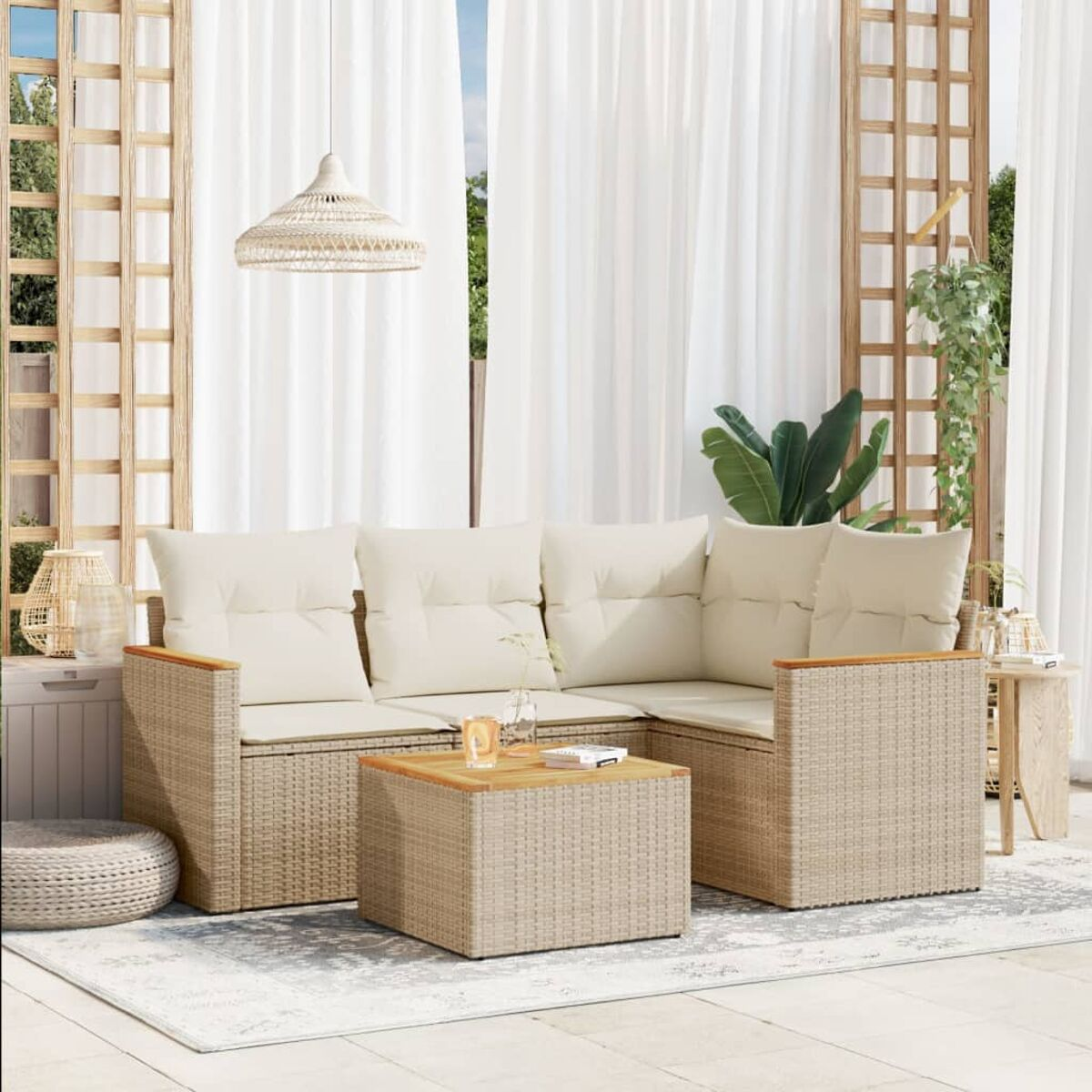 Geflochtenes Outdoor-Sofa mit cremefarbenen Kissen und einem Couchtisch, auf einer Terrasse mit Vorhängen und Pflanzen.