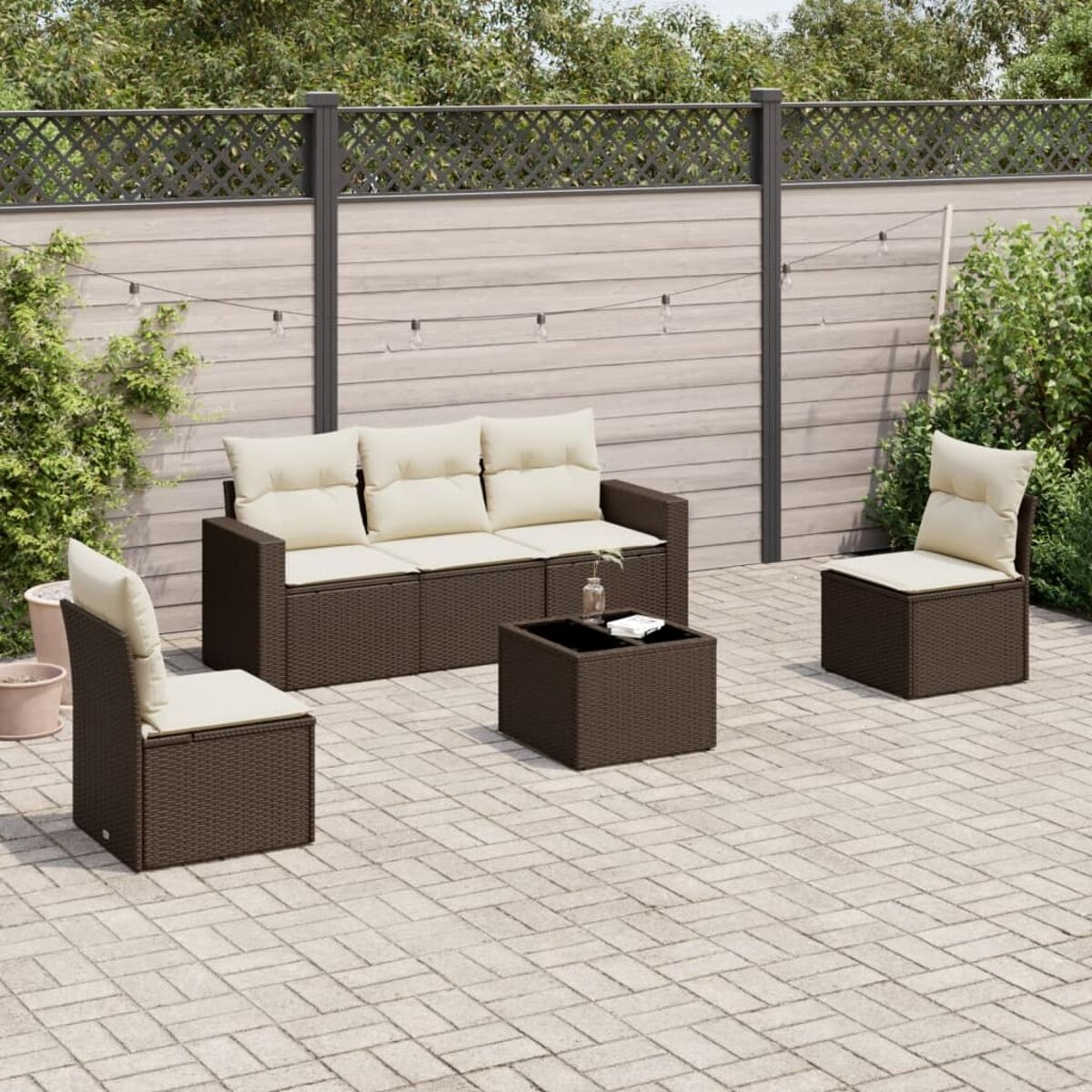 Set divano in rattan con cuscini beige su un patio in mattoni. Un bicchiere d'acqua sul tavolo.