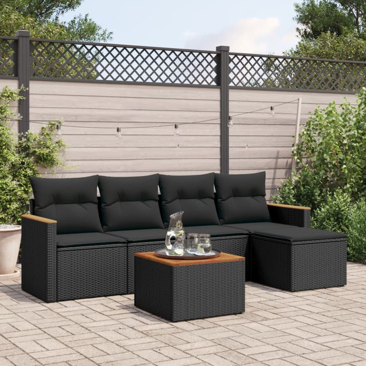 Schwarzes Ecksofa-Set aus Weide mit schwarzen Kissen, Holztisch und Backsteinterrasse.