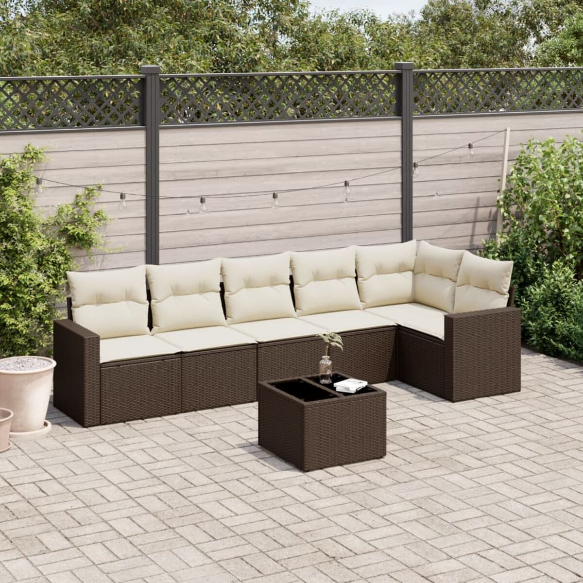 Divano componibile in rattan marrone con cuscini color crema e un tavolino su un patio in mattoni.