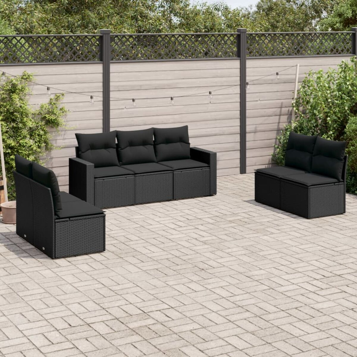 Schwarzes Gartenmöbel-Set aus Korbgeflecht mit schwarzen Kissen auf einer gepflasterten Terrasse.