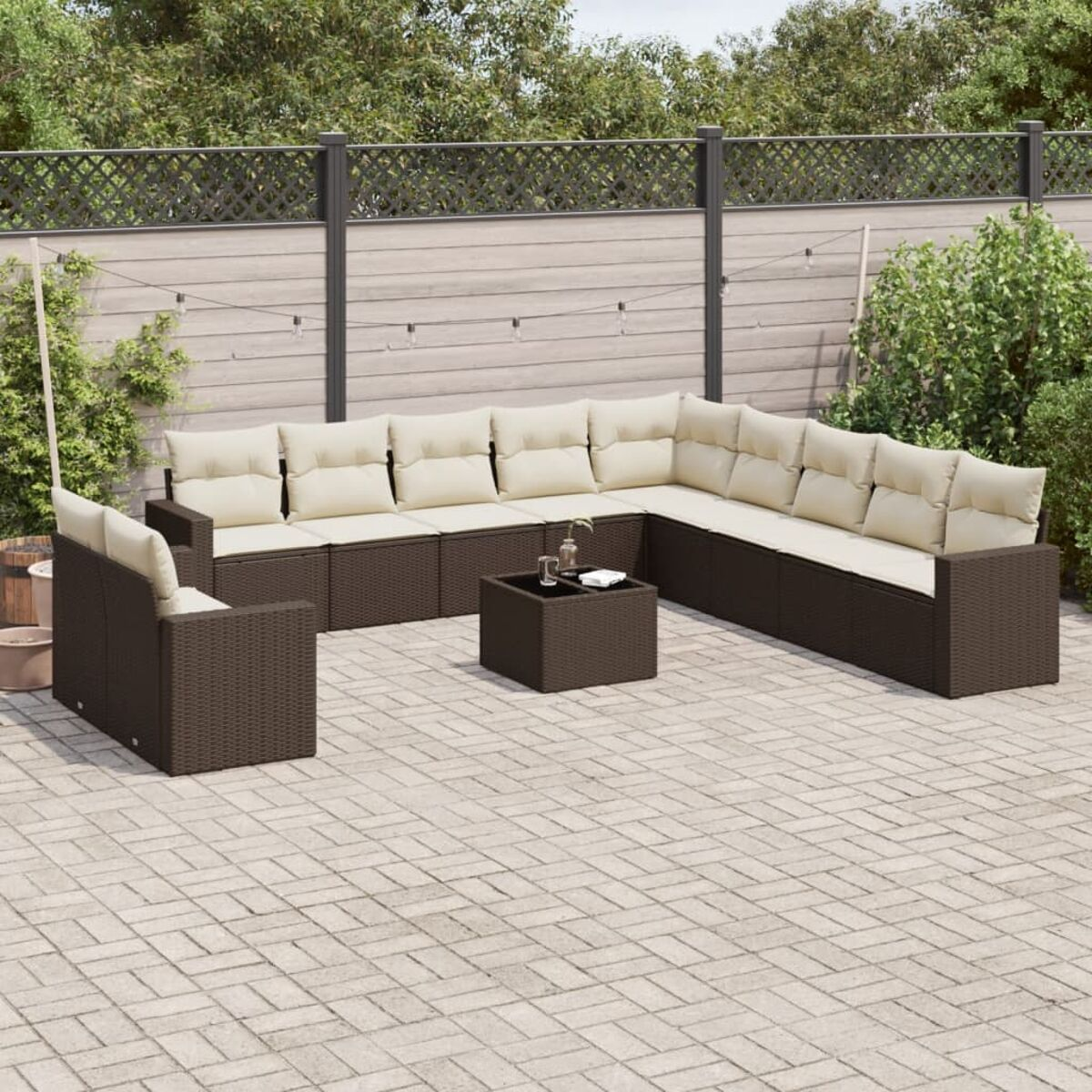 Set da patio in vimini marrone con cuscini beige. Patio in pietra con piante verdi e recinzione in legno.