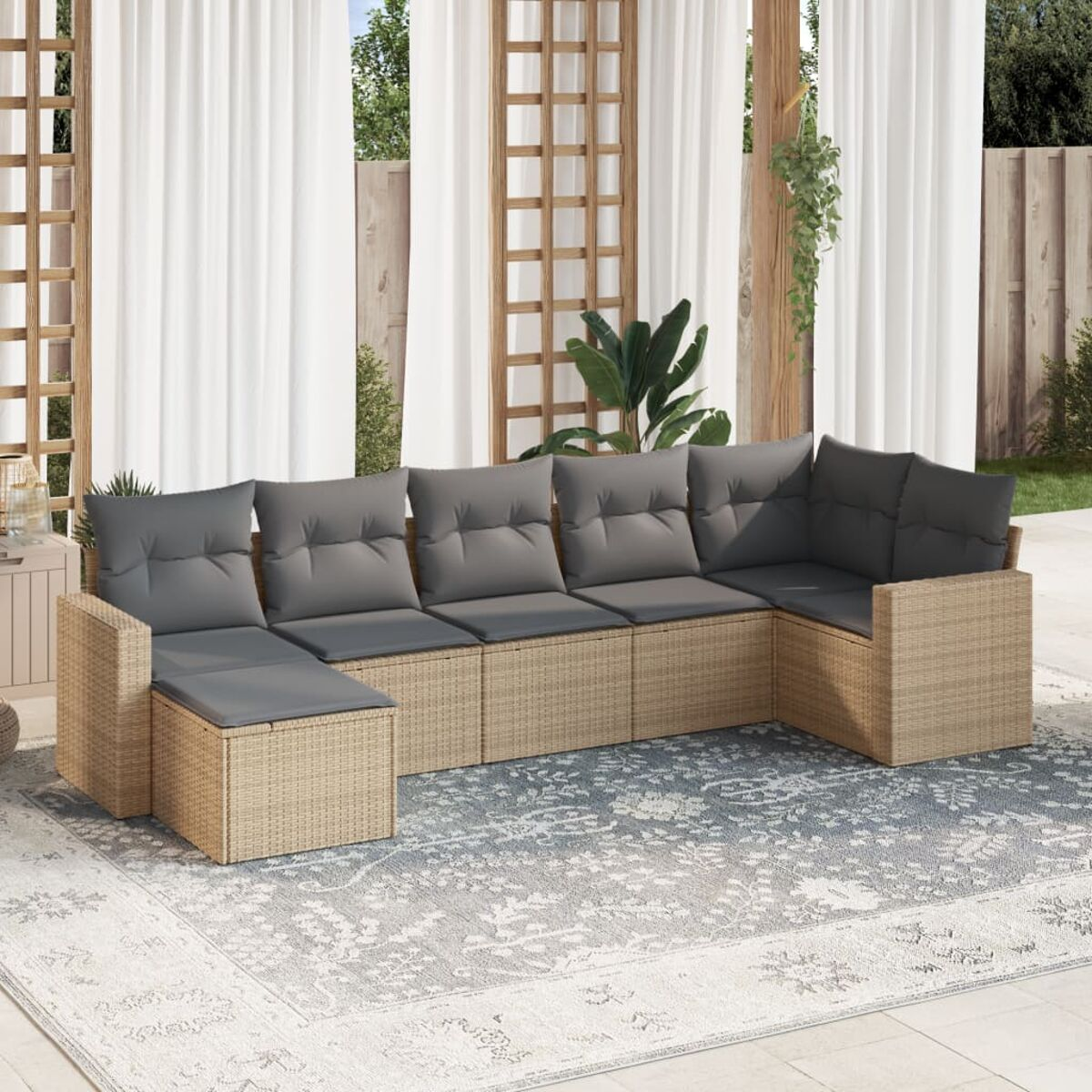 Sofa aus Korbgeflecht mit grauen Kissen auf gemustertem Teppich, weiße Vorhänge im Hintergrund.