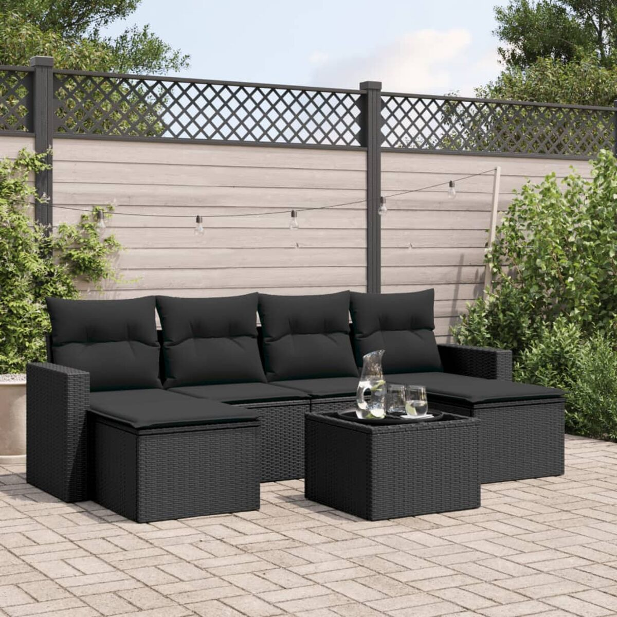 Schwarzer Outdoor-Schnitt mit Kissen und einem Tisch auf einer Terrasse. Grün und Zaun im Hintergrund.