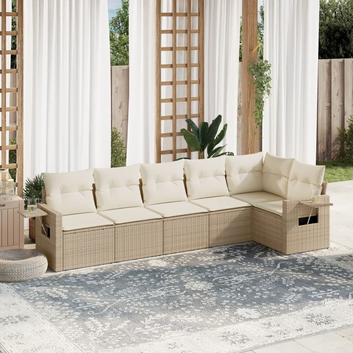 Ein beiges Rattan-Ecksofa mit cremefarbenen Kissen steht in der Nähe eines Tisches. Vorhänge und Pflanzen im Hintergrund.