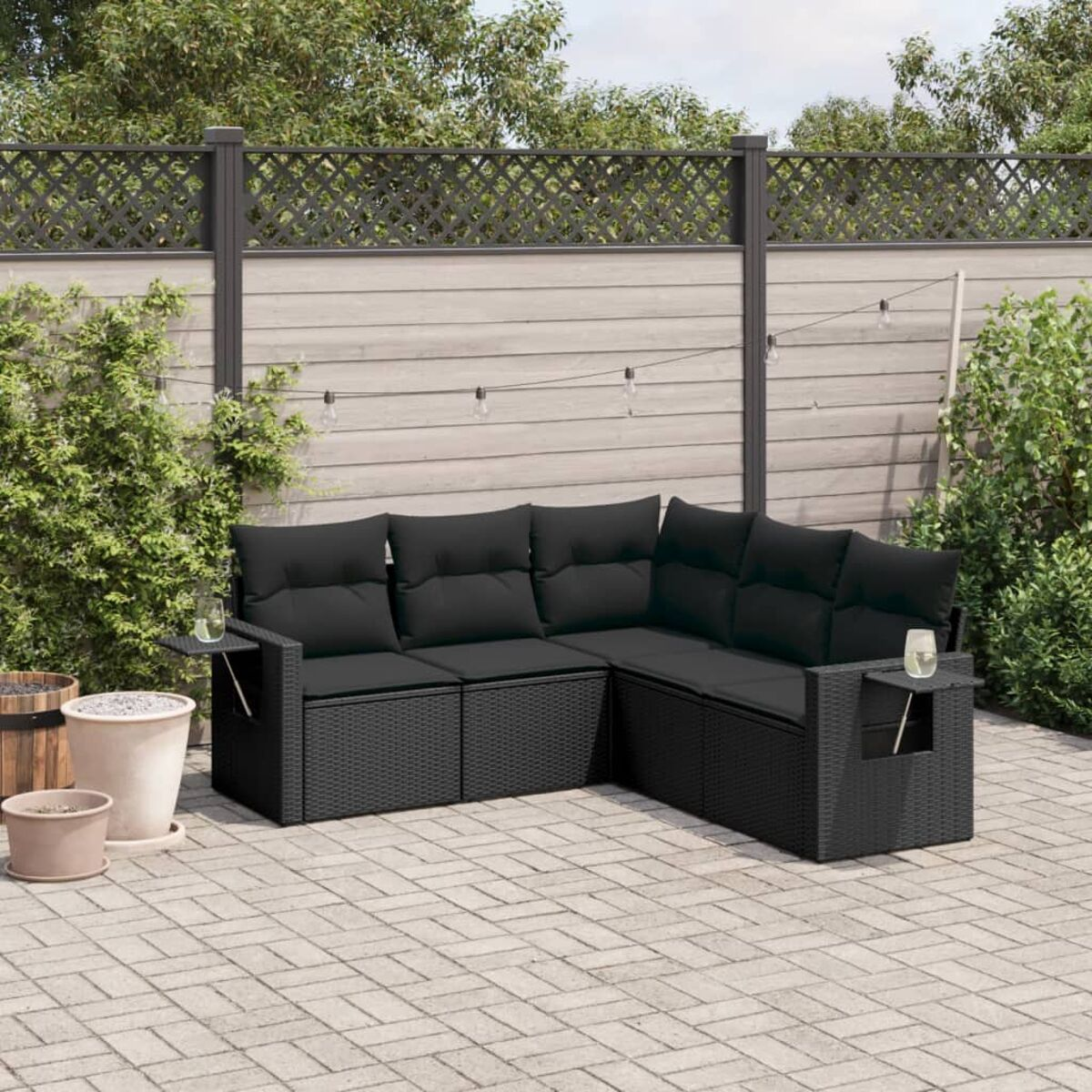 Schwarzes Outdoor-Sofa-Set auf einer gepflasterten Terrasse mit Pflanzen und Zaun.