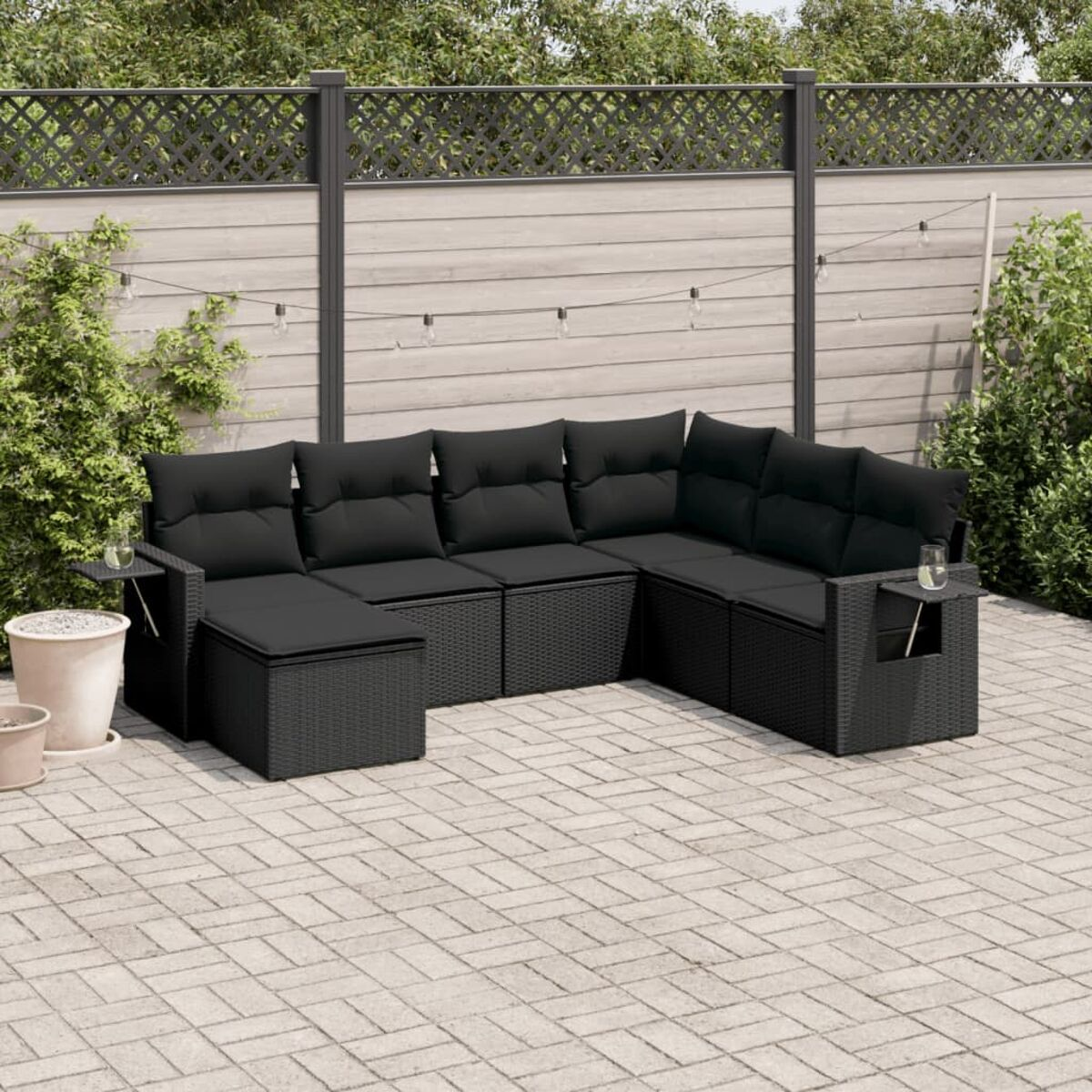 Schwarzes Outdoor-Ecksofa aus Korbgeflecht mit schwarzen Kissen und Beistelltischen. Terrasse.