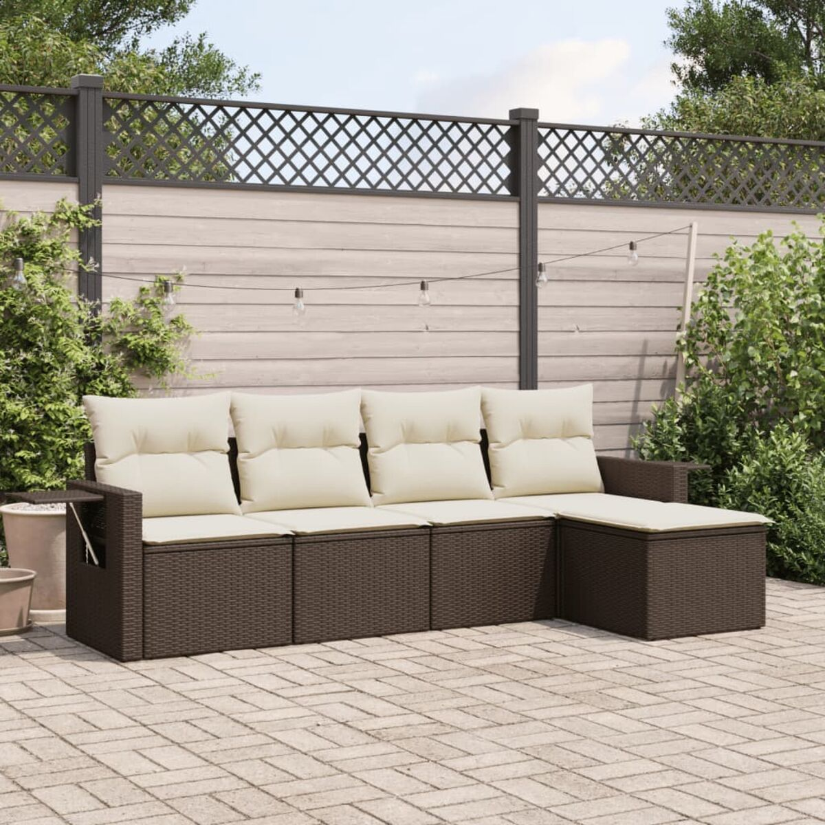 Braunes Outdoor-Ecksofa aus Korbgeflecht mit cremefarbenen Kissen. Backstein-Patio mit Zaun im Hintergrund.