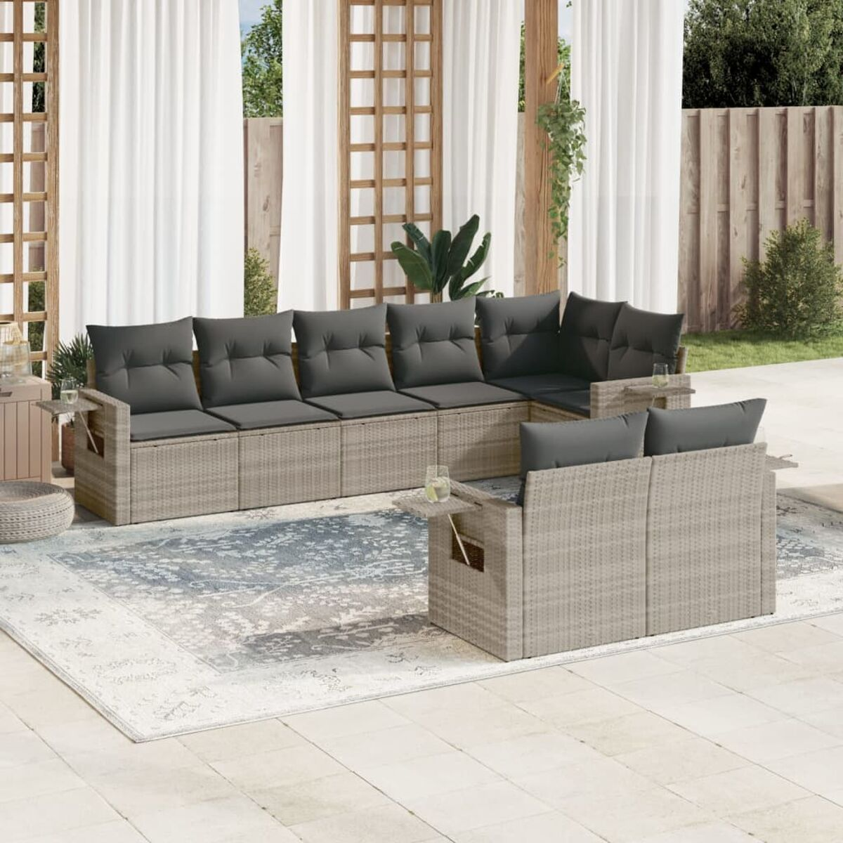 Rattansofa für draußen mit grauen Kissen, einem Teppich und weißen Vorhängen.
