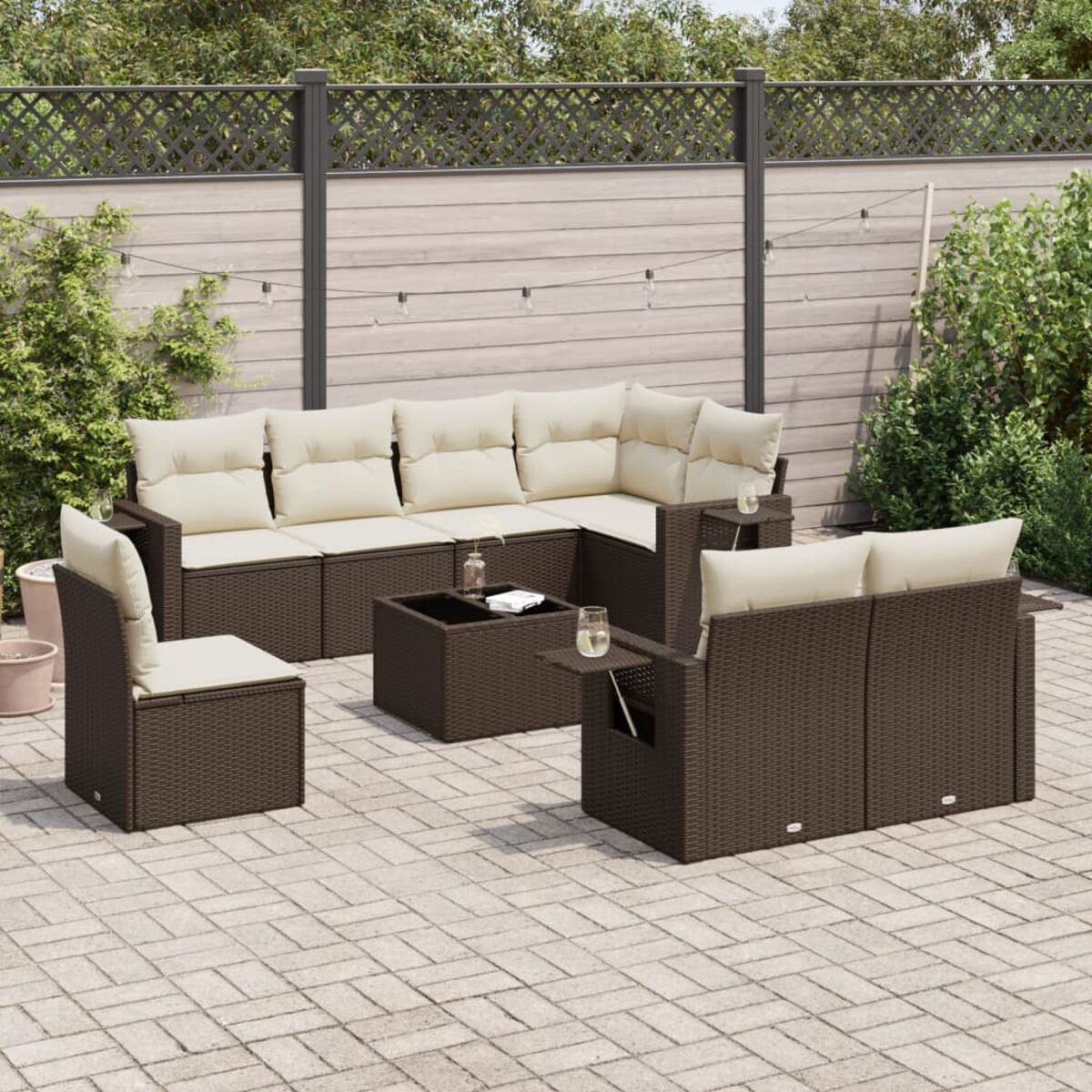 Divano componibile marrone per esterni con cuscini color crema, tavolino e sedia su un patio. Recinzione e luci.