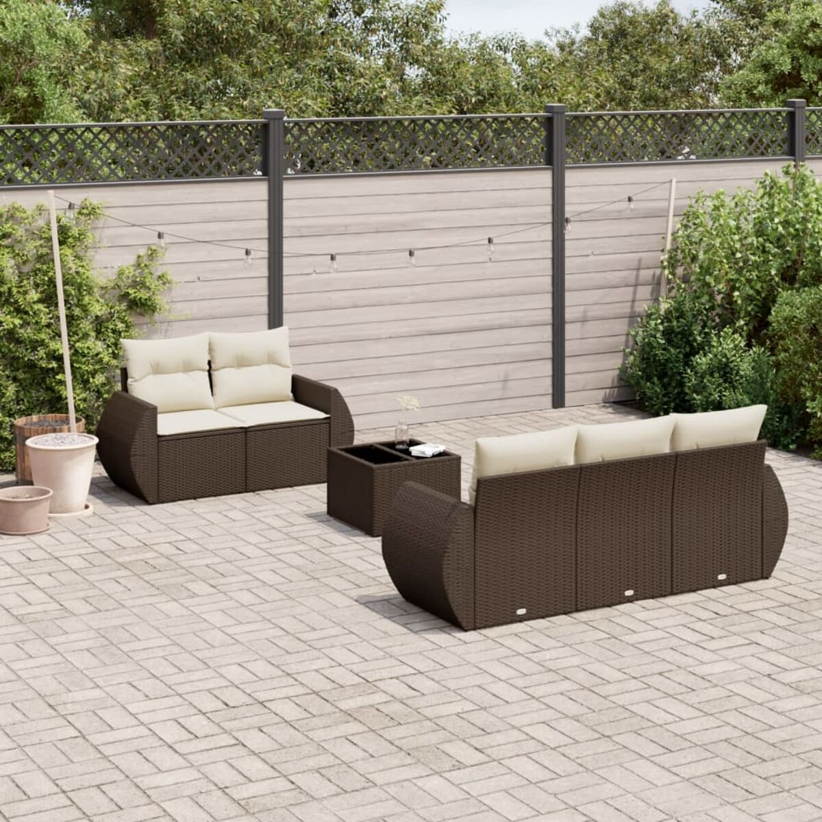 Outdoor-braune Korbsessel mit cremefarbenen Kissen und einem Couchtisch auf einer Ziegelterrasse mit schwarzem Zaun.