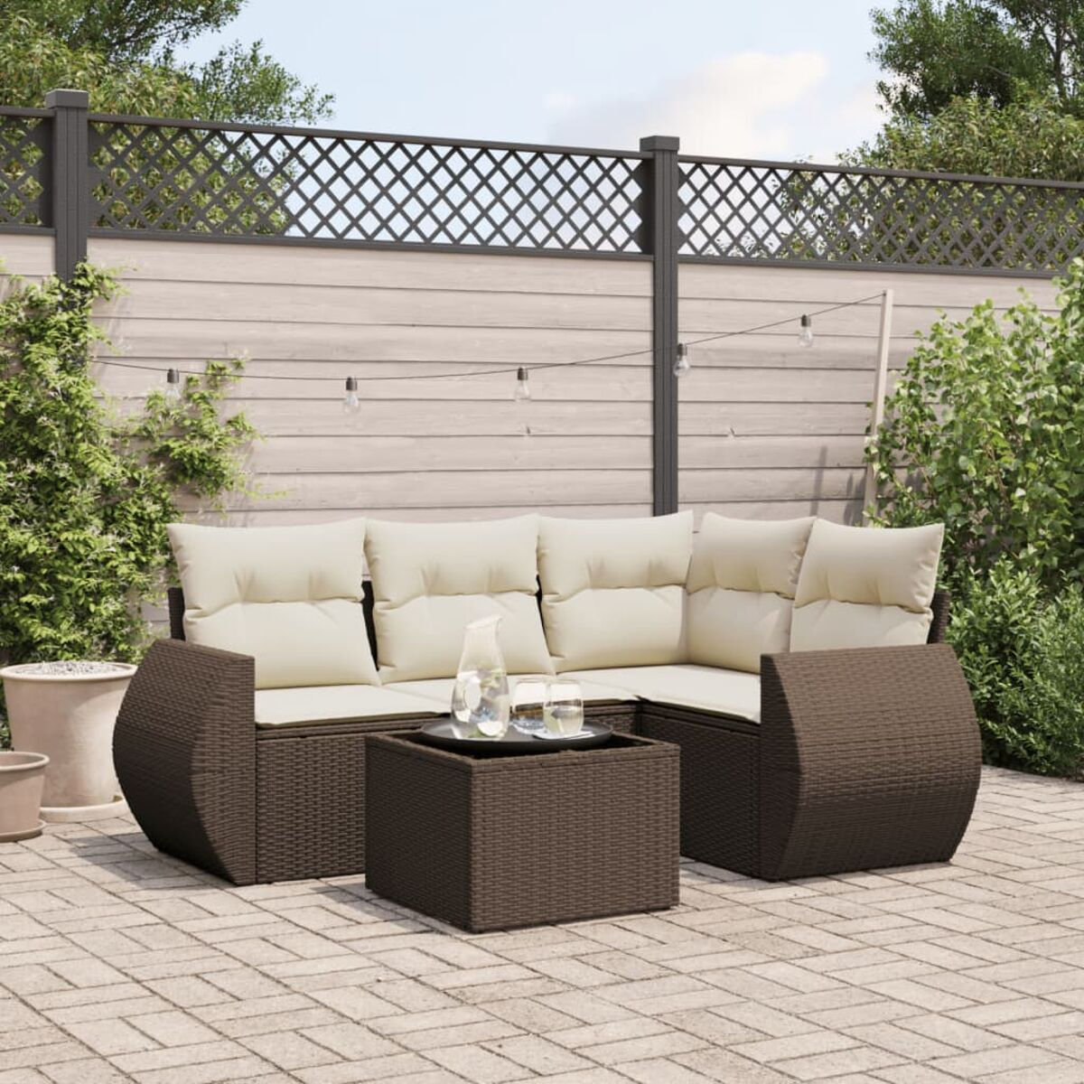 Divano angolare in rattan marrone con cuscini color crema e un tavolo con bicchieri e una brocca d'acqua.