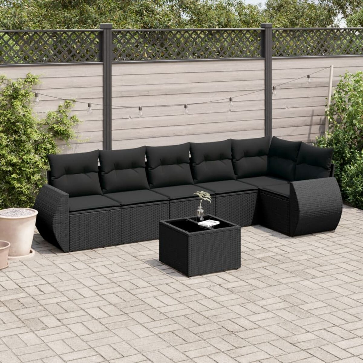 Schwarzes Rattan-Ecksofa mit Kissen und ein schwarzer quadratischer Couchtisch auf Ziegelpflaster.