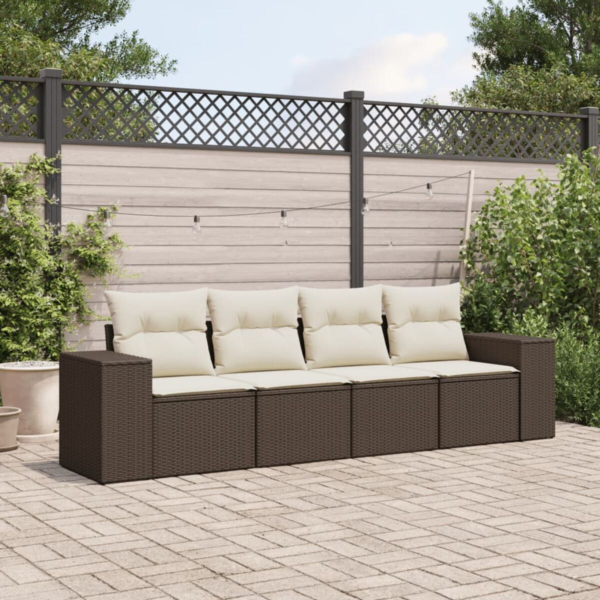 Braunes Rattan-Sofa mit cremefarbenen Kissen, auf einer Backsteinterrasse, mit Zaun und Lichterketten.