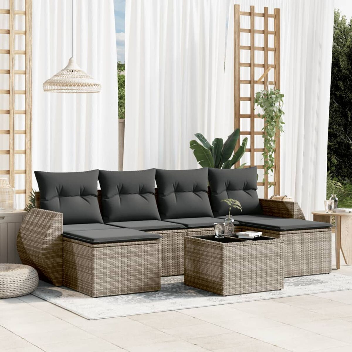 Ein Korbmöbel-Sofa-Set mit grauen Kissen und einem Tisch auf einem Teppich draußen.