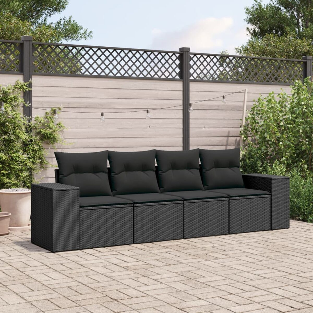 Schwarzes Outdoor-Sofa aus Korbgeflecht mit schwarzen Kissen. Es befindet sich auf einer Backstein-Terrasse mit eingezäuntem Hintergrund und Pflanzen.