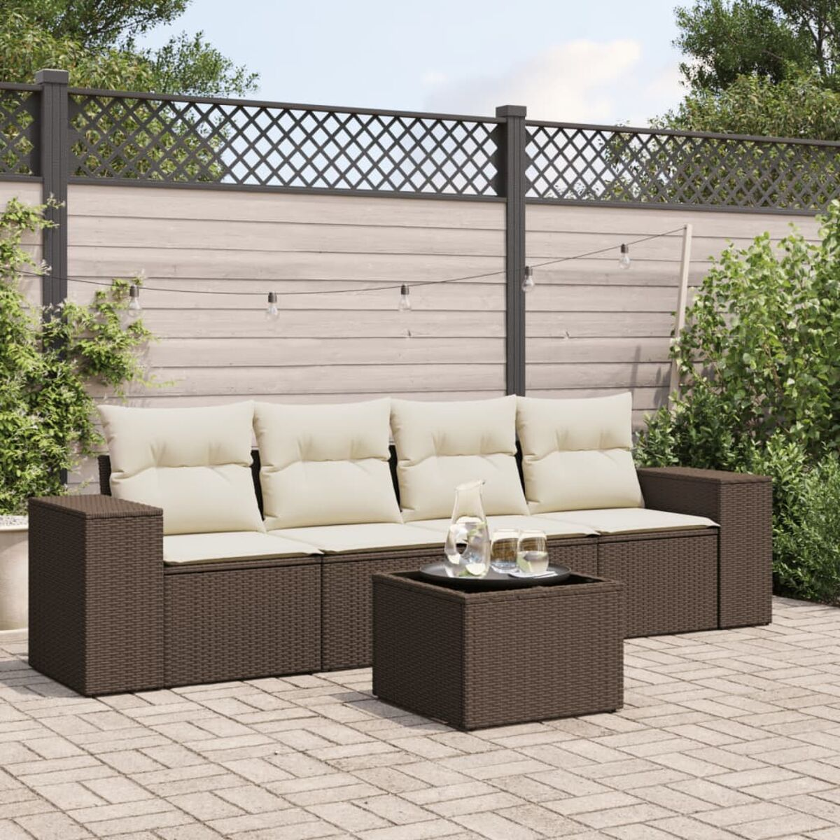 Brauner Outdoor-Wicker-Schnitt mit cremefarbenen Kissen und einem Tisch auf einer Terrasse, mit Grün und Zaun im Hintergrund.