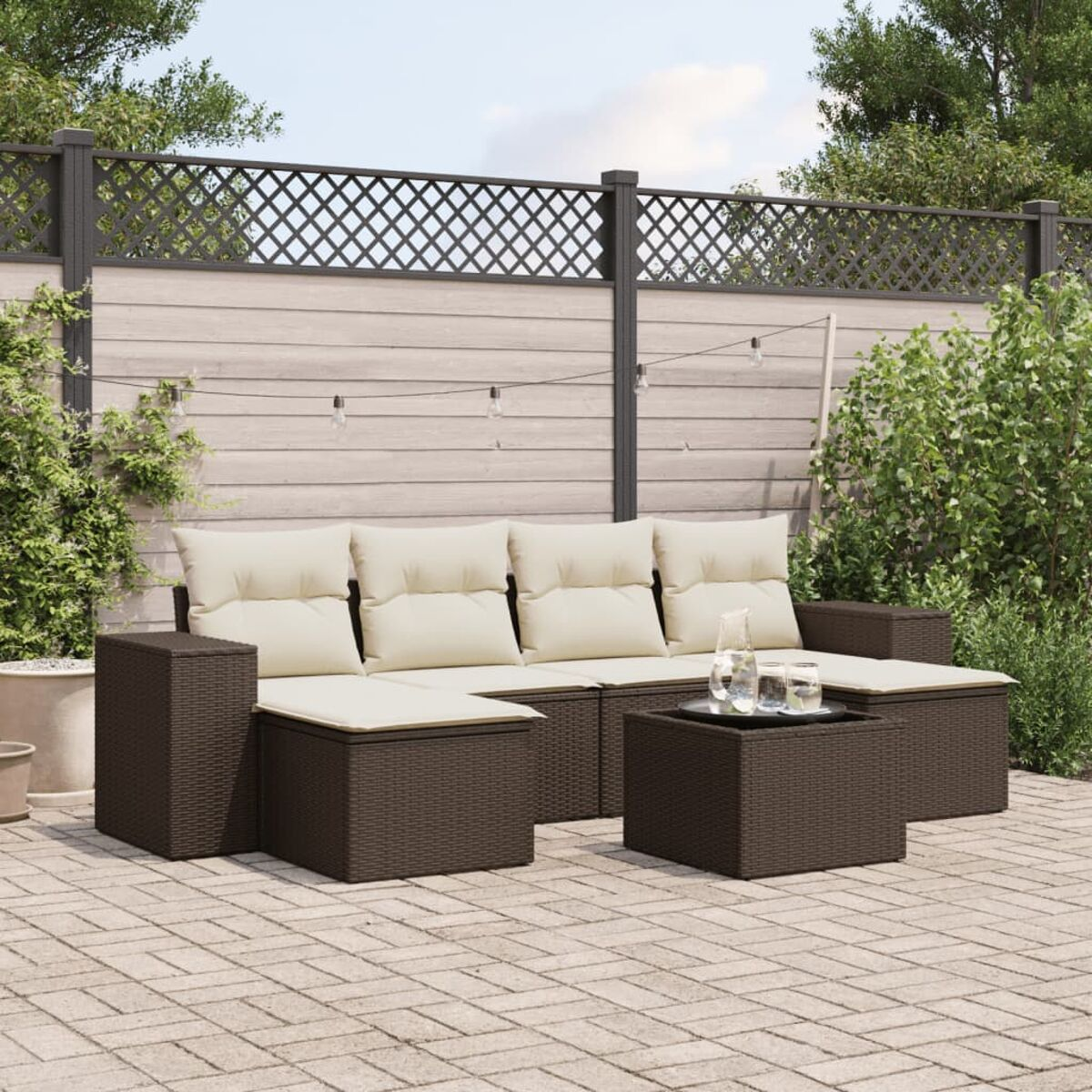 Divano angolare marrone scuro con cuscini color crema e un tavolino su un patio. Recinzione e luci sullo sfondo.