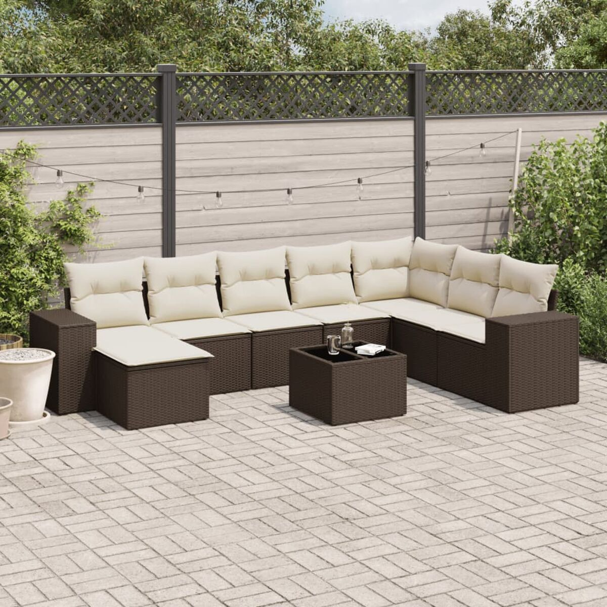Braunes Rattan-Ecksofa mit beigen Kissen und Tisch auf Terrasse, Holzzaun im Hintergrund.